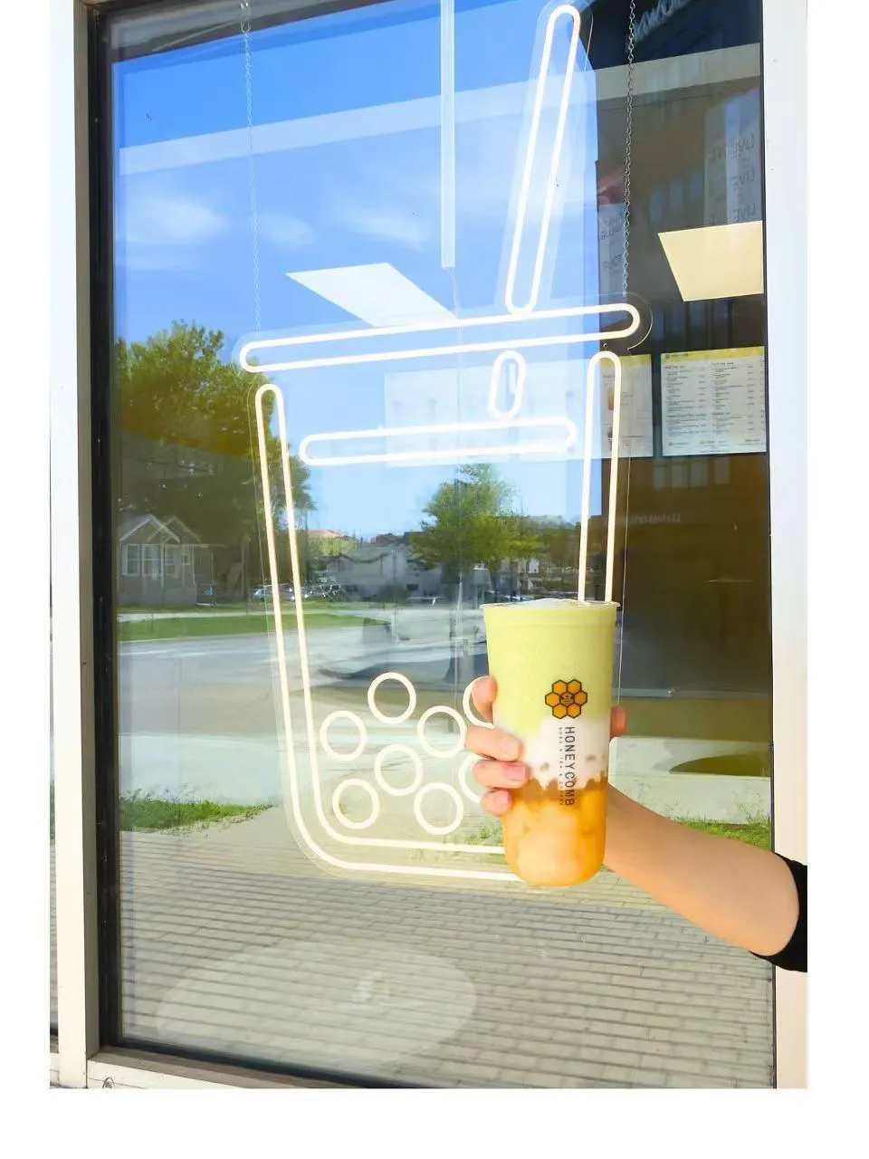 Hand Holding a Honeycomb Mango Matcha Boba Tea in Front of a Bubble Tea Neon Window Sign